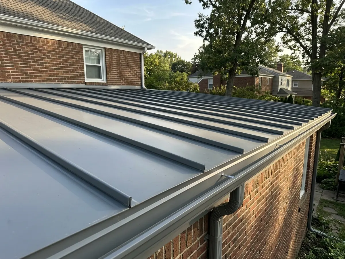 Grey standing seam panels with tall folded double-lock seams on a nearly flat rear addition roof
